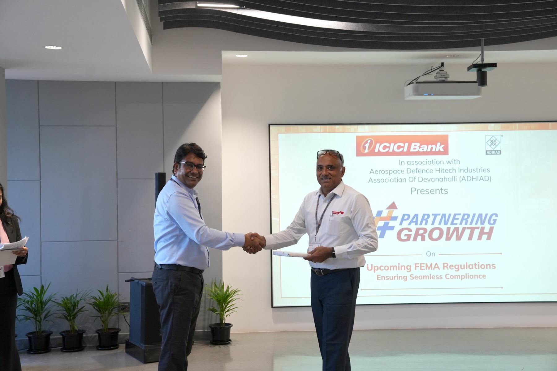 Speakers exchange a token of appreciation in front of the Partnering Growth and Upcoming FEMA Regulations screen.